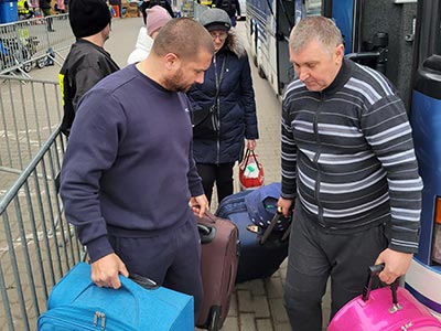 Jeff and bus driver carry suitcases of refugees to bus